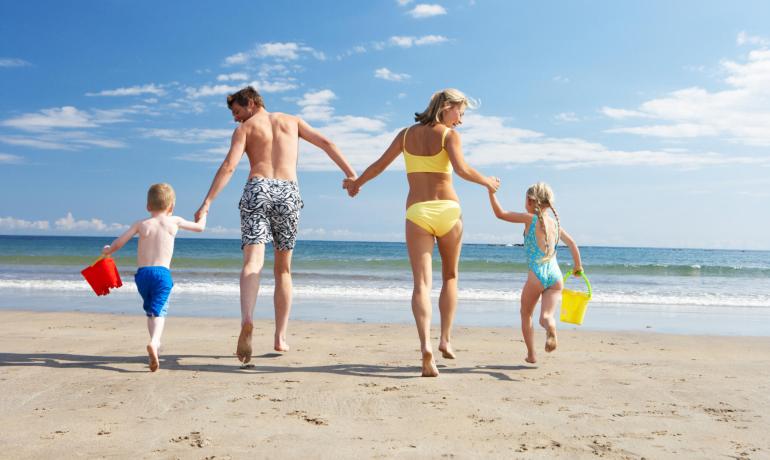 Famiglia felice corre sulla spiaggia con secchielli colorati.